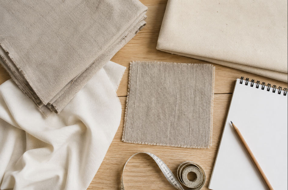 Fabric swatches, measuring tape, and notes arranged on a worktable for comparing linen and cotton before choosing yardage.