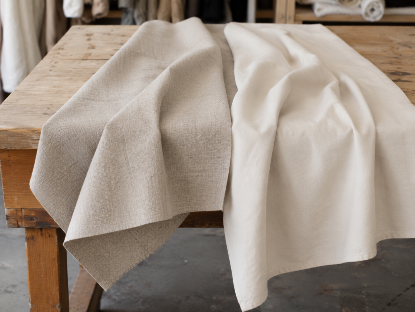 Linen and cotton fabric swatches draped over a table edge to compare crisp linen structure with softer cotton drape.