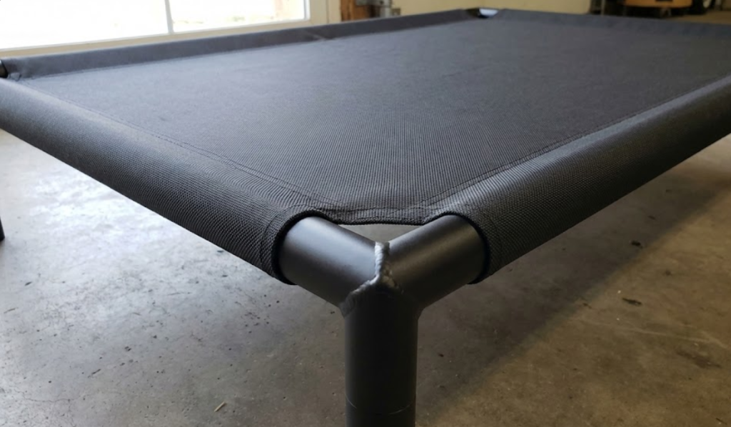 Heavy-duty ballistic nylon fabric pulled taut over an elevated aluminum dog cot frame to eliminate loose chewing targets and prevent seam failure.