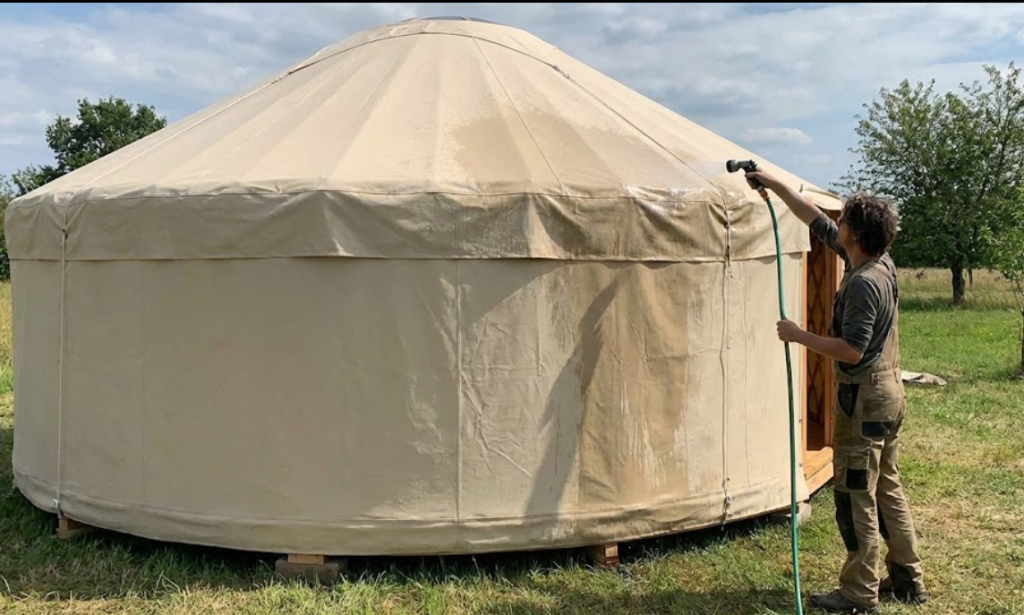 Person applying water to a newly installed yurt canvas cover to induce hygroscopic swelling and weather the fabric.
