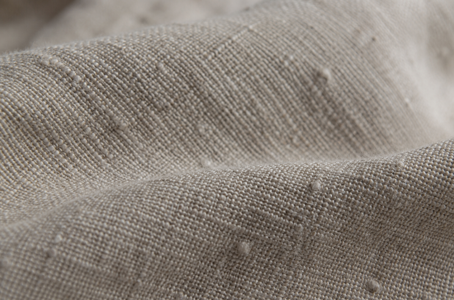 Macro view of natural linen fabric showing visible weave texture, slub, and thick-thin yarn variation