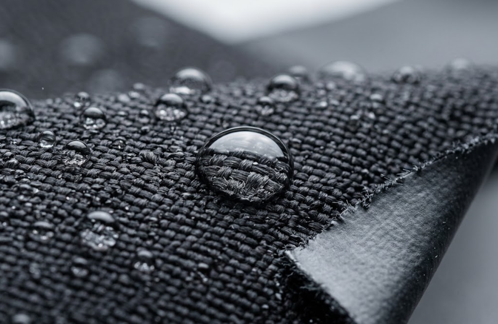 ater droplets beading on the DWR-treated surface of ballistic nylon fabric with exposed edge revealing the polyurethane moisture barrier back-coating.