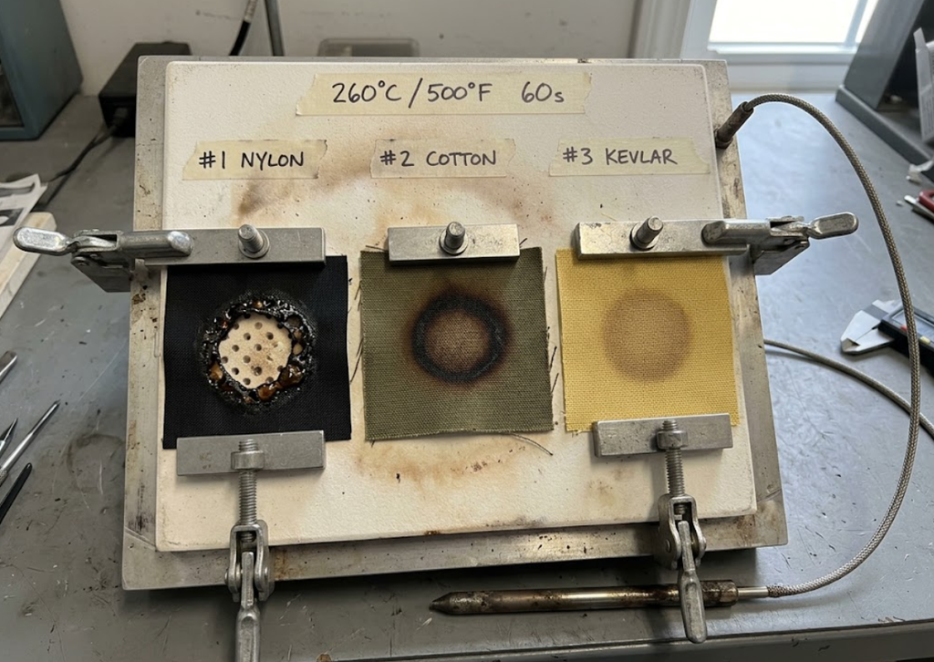 Thermal contact test comparison showing synthetic nylon melting into a hole at 255 degrees Celsius versus heavy cotton duck canvas with safe surface charring and intact yellow Kevlar.